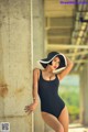 A woman in a black bathing suit leaning against a wall.