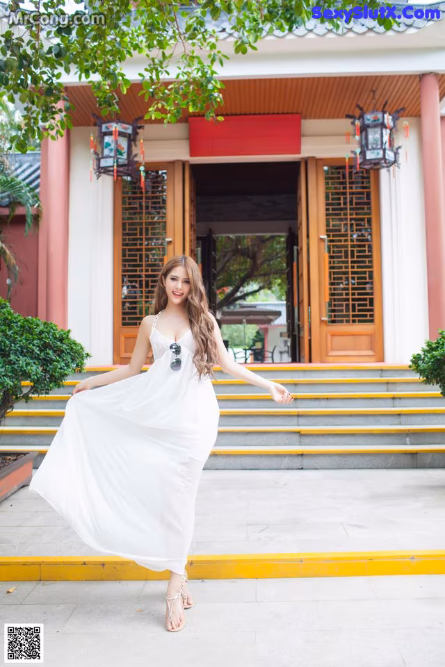 A woman in a white dress standing in front of a building.