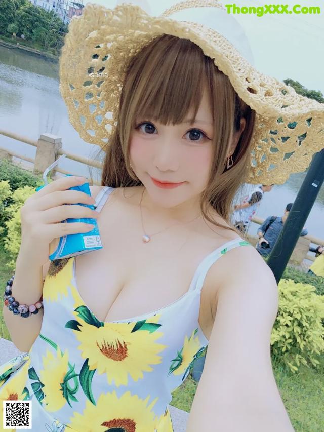 A woman in a sunflower dress and straw hat taking a selfie.