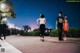 A woman jogging down a sidewalk at night with a man and a woman in the background.