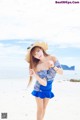 A woman in a blue dress and hat on a beach.