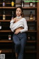 A woman sitting on a stool in front of a shelf of liquor bottles.