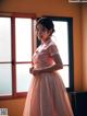 A woman in a pink dress standing in front of a window.