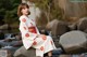 A woman in a white kimono sitting on a rock by a stream.