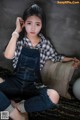 A young woman sitting on a couch wearing overalls.