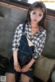 A woman sitting on a couch wearing overalls and a plaid shirt.