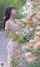 A woman in a floral dress standing next to a bush of flowers.