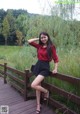 A woman in a red shirt and black skirt posing on a wooden bridge.