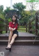 A woman in a red shirt and black skirt sitting on a wooden deck.