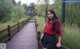 A woman in a red shirt and black shorts standing on a wooden bridge.