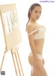 A woman in a white lingerie standing next to an easel.